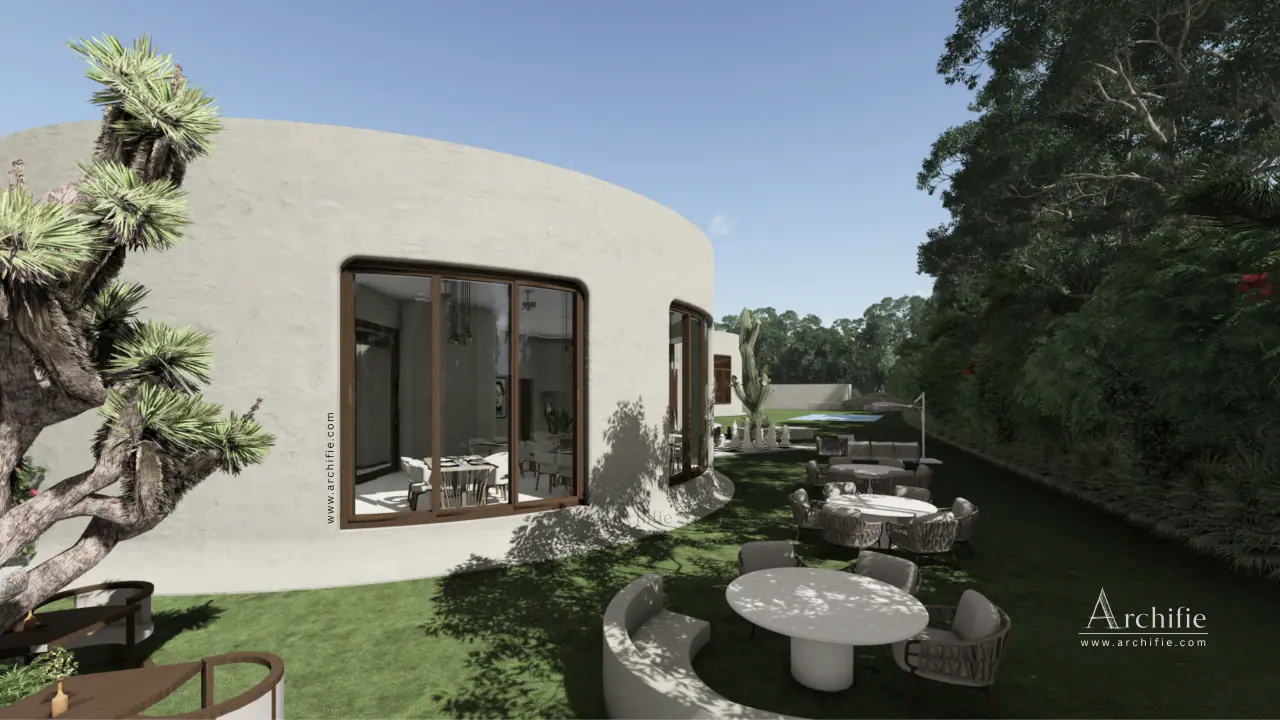 Alfresco tables on the lawn beside the curved restaurant in daylight, a sculptural tree at the corner